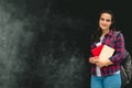 Woman wearing casual shirt and jeans and backpack holding books on a background of chalkboard with place for text