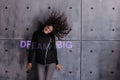 Curly young woman with flying hair actively posing on the background of concrete wall. A colored illuminated Dream big.