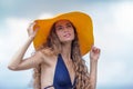 Curly young woman in yellow board brim hat poses with arms raised and looks up