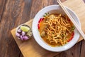 Curried noodle soup Khao soi with chicken meat and spicy coconut milk on wood table.