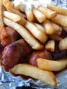Currywurst & Pommes: Famous German Fast Food Curry Sausage with French Fries and Curry Sauce on aluminium foil Royalty Free Stock Photo