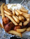 Currywurst & Pommes: Famous German Fast Food Curry Sausage with French Fries and Curry Sauce on aluminium foil Royalty Free Stock Photo