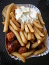 Currywurst & Pommes: Famous German Fast Food Curry Sausage with French Fries and Curry Sauce on aluminium foil Royalty Free Stock Photo