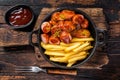 Currywurst Sausages with Curry spice on wursts served French fries in a pan. Dark wooden background. Top view