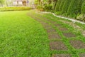 Curve pattern walkway of square Laterite stepping stone on fresh green grass yard, smooth carpet lawn, brown gravel and concrete Royalty Free Stock Photo