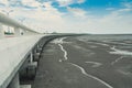 Curved coastal concrete highway road with lower water in the mud beach with blue sky and clouds. Road trip travel. Summer journey