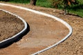 Curved concrete curb at local sidewalk construction site filled with gravel and small grain sand surrounded with grass and trees Royalty Free Stock Photo