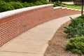 Curved descending sidewalk ramp flanked on one side with a clean, well maintained brick retaining wall, neat bushes and landscapin Royalty Free Stock Photo