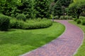 Curved pathway paved brick stone tiles in park among plants. Royalty Free Stock Photo