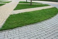 curved pedestrian pavement of stone tiles in park with slope landscape lighting and green plants on flower bed, meadow of on turf