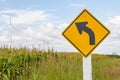 Curved road traffic sign with windmill background in wind farm.