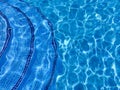 Curved steps into swimming pool, view from above through water on blue mosaic tiles. Waves on water surface. Distortion. Royalty Free Stock Photo