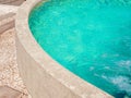 Curved stone edge design of the poolside near aqua blue water pool background with water pressure splashing.