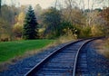 Curved train tracks, evergreens, birch, manicured green lawn