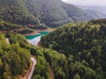 Curving road section running along lake with turquoise water and the green woods of high mountains