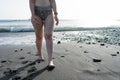 Curvy adolescent walking in the beach in the sunset in the wet black sand and waves on the sea. Caucasian woman in bikini at the Royalty Free Stock Photo