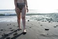 Curvy adolescent walking in the beach in the sunset in the wet black sand and waves on the sea. Caucasian woman in bikini at the