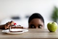 Curvy African American woman choosing between cake and apple, peeking at food from under table, free space Royalty Free Stock Photo