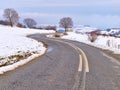 Curvy asphalt road  bare trees and cloudy sky, snow winter landscape Royalty Free Stock Photo