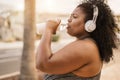 Curvy black woman drinking water after jog routine outdoor at city park - Focus on face