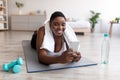 Curvy black woman using smartphone during break from home training, browsing internet, looking up workout video online