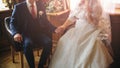 Curvy bride in white lace dress is holding hands with her groom. Wedding couple sitting on the vintage chairs. Happy ceremony. Royalty Free Stock Photo