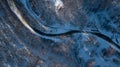 Curvy windy road in snow covered forest, top down aerial view.