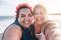 Curvy women friends taking selfie on the beach with sunset in background - Happy plus size body female having fun together - Royalty Free Stock Photo