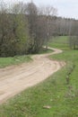 Curvy zigzag gravel road through the trees and bushes on one side and green meadow on the other in Lithuania Royalty Free Stock Photo