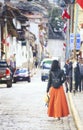 Cusco County, Peru - August 8th, 2018: A woman wearing an orange skirt and a hat walks on the steet in a old town of Cusco area in