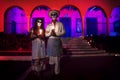 costumed man and woman with with mexican traditional white clothes and scarves and skull make-up in front of red pink lightened bu Royalty Free Stock Photo