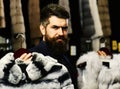 Customer with beard chooses furry coats. Man with strict face