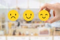 Hand choosing smile emotion icons for giving best service ranking with blurred front view of cafe restaurant or coffee shop.