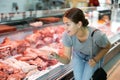 Customer girl looks at glass display case of refrigerator and chooses pork wing ribs