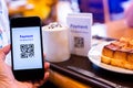 Customer hand using smart phone to scan QR code tag with blur coffee and bread set meal in coffee shop or restaurant to accepted