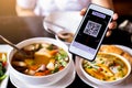 Customer hand using smart phone to scan QR code tag with blurry Thai food to accepted generate digital pay without money
