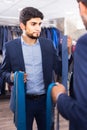 Customer man is picking up tie for jacket in front of the mirror