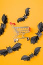 The customer's toy cart is located in the middle of paper decorative bats. Orange background. Vertical. Flat lay. Royalty Free Stock Photo