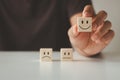 Customer satisfaction concept. Customer's hand lifts smiling face on blurred sad face icon on wooden cube block