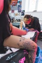 a customer sitting on a table and a tattoo artist making a new tattoo on her leg, vertical shot Royalty Free Stock Photo