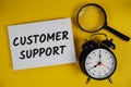 Customer Support letters with magnifying glass and alarm clock flat lay on yellow background Royalty Free Stock Photo