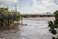 Customers sitting on metal resturant balcony over muddy flooded river with bridge and power plant in distance