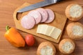 Cut cheese and ham on a wooden board, knife, buns, tomato, pepper Royalty Free Stock Photo
