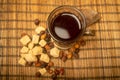 A cut-glass Cup of tea in a vintage Cup holder, dried rosehip fruit and chunks of brown cane sugar on a cane Mat. Close up Royalty Free Stock Photo