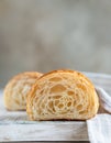 Cut in half croissant with inside texture and thin crisp layers on wooden board, light background. Delicious french pastry