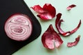 A cut half of a red onion lies on a black and light green background next to a peeled onion husk Royalty Free Stock Photo