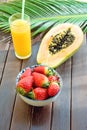 Cut in Half Ripe Papaya Fresh Strawberries Tropical Juice in Tall Glass with Straw Palm Leaf on Plank Wood Table in Cafe Royalty Free Stock Photo