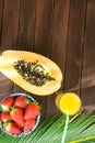 Cut in Half Ripe Papaya Fresh Strawberries Tropical Juice in Tall Glass with Straw Palm Leaf on Plank Wood Table Top View Royalty Free Stock Photo