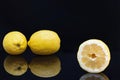 A cut lemon in the foreground with two more lemons on black background