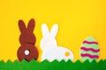 Cut out of felt applications of easter egg and white and brown rabbits on the grass. Yellow background. Rear view. Flat lay. Royalty Free Stock Photo